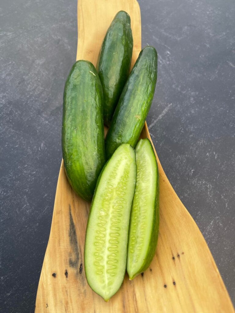 One half and three Cengelkoy cucumbers photographed in a long, wooden container, photographed on a background with marble pattern.