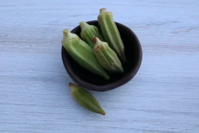 Cicek Çiçek okra pods photographed in a small clay bowl and backdrop with wood pattern.