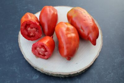 WV Pepper Three whole and one half West Virginia Pepper tomatoes are lying on a piece of wood slice.