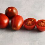 Three whole and one half Black Plum tomato fruits photographed on backdrop with marble pattern.