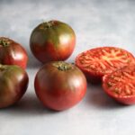 Four whole and one half Black Krim purple tomatoes pictured on photography background.