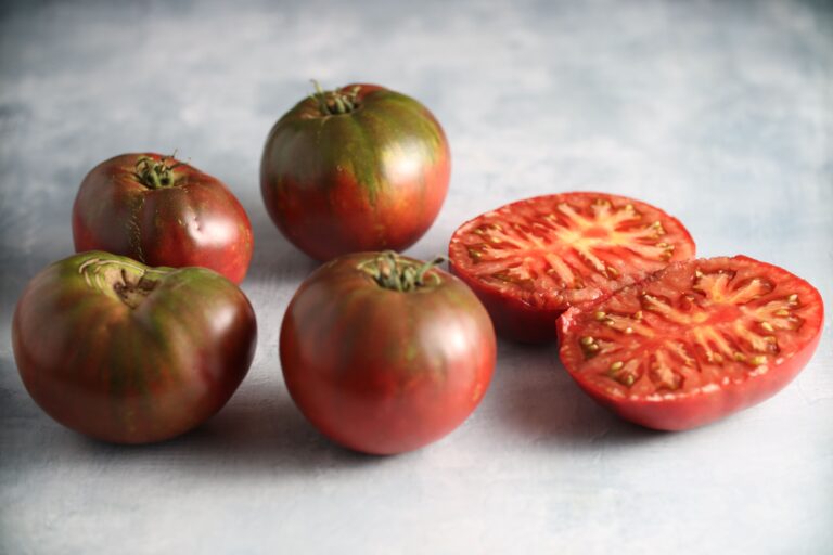 Tomato Seeds, Black Krim Four whole and one half Black Krim purple tomatoes pictured on photography background.
