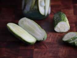 Sliced and halved Boston Pickling cucumber fruits photographed on a backdrop with wood texture.