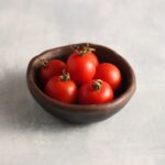 Peacevine cherry tomato fruits are photographed in a small clay bowl that is on a backdrop with marble pattern.