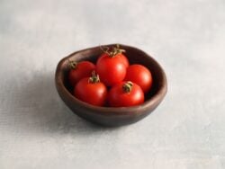 Peacevine cherry tomato fruits are photographed in a small clay bowl that is on a backdrop with marble pattern.