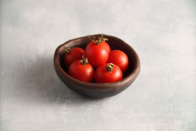 Peacevine Cherry1 Peacevine cherry tomato fruits are photographed in a small clay bowl that is on a backdrop with marble pattern.