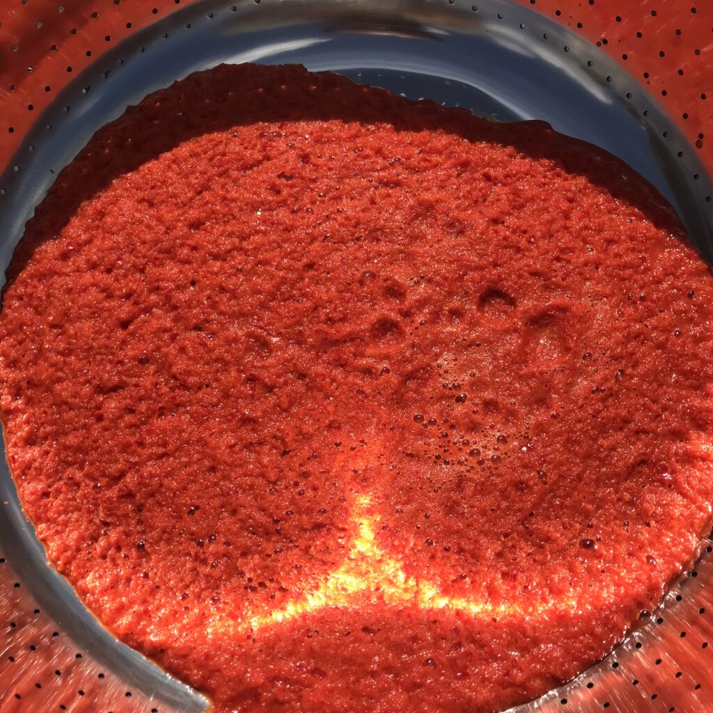 Second step for making Turkish pepper paste is to run the pulp through a colander to remove the coarse parts of the pulp.